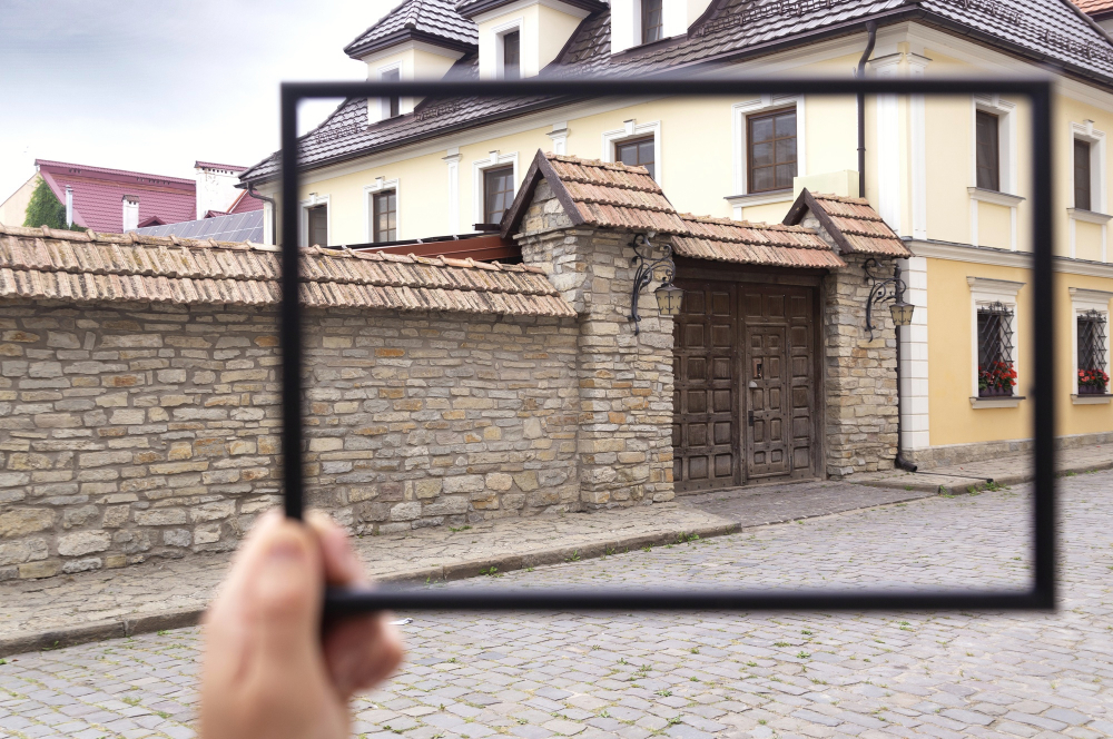 Ein Haus im Blick: Hand hält einen Rahmen vor ein Steinhaus mit Holztor